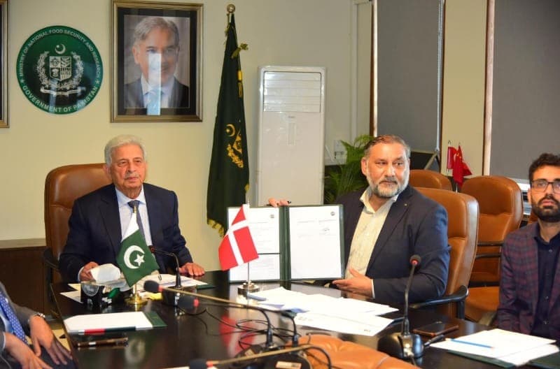 The signed documents displayed at the Ministry table beside the flags of Pakistan and Denmark.